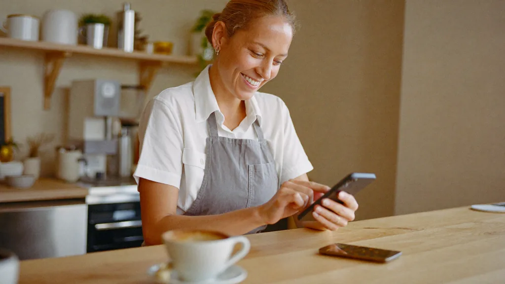 Eine Restaurantinhaberin liest am Tresen auf dem Smartphone ihre Google-Bewertungen und antwortet darauf